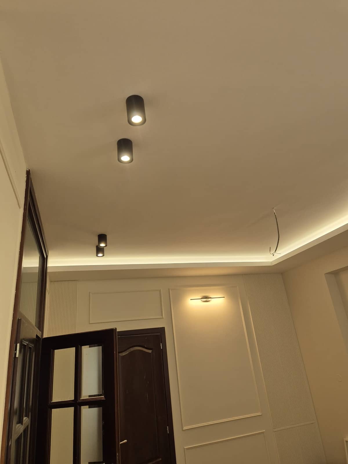 Ista soba posle radova, ista vrata: zidna LED lampa na panelu, crne spot lampe i indirektno svetlo u spuštenom plafonu