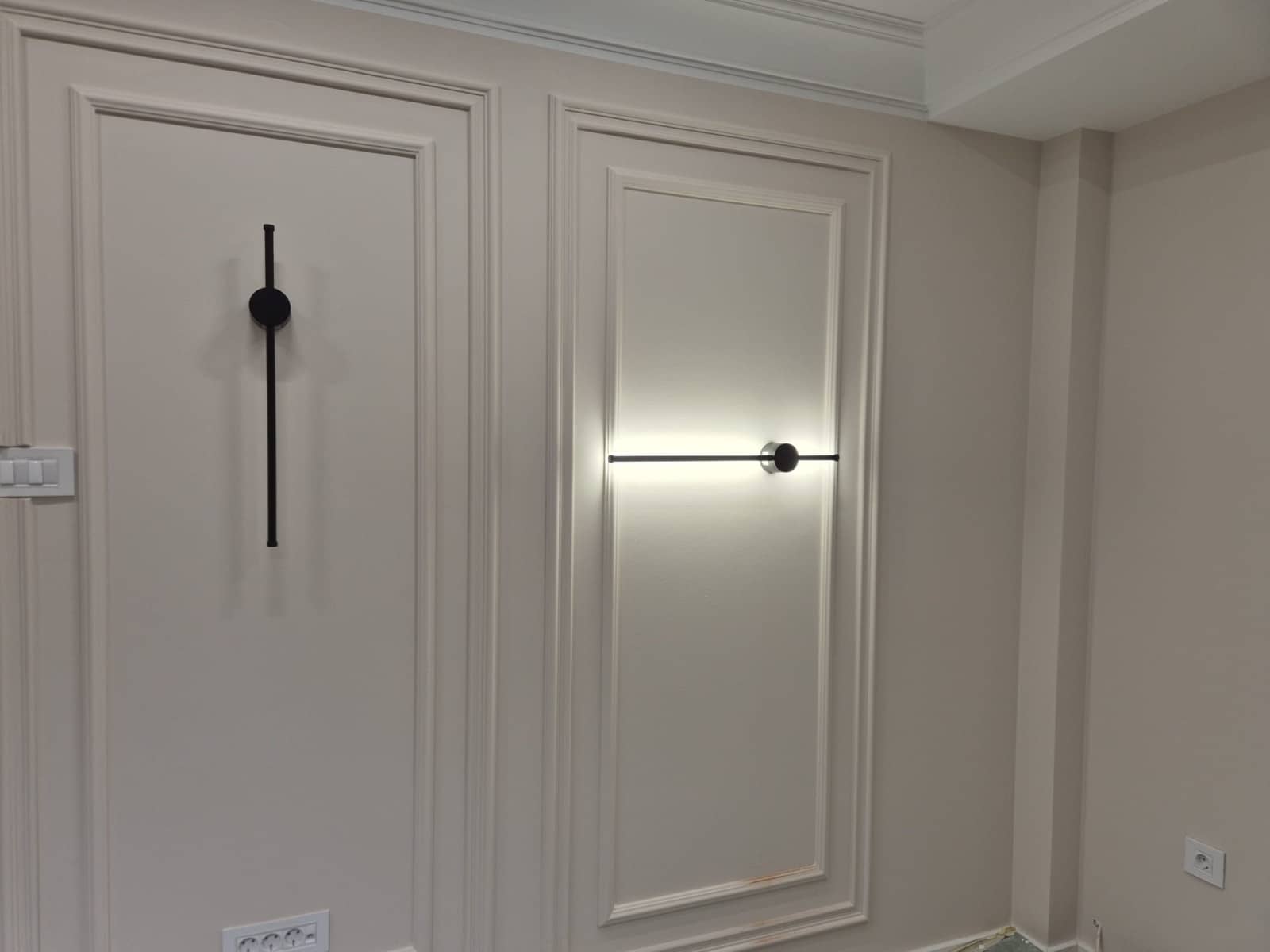 Zidni paneli sa dve linijske LED lampe, jedna uključena, i uredno postavljenim prekidačima i utičnicama